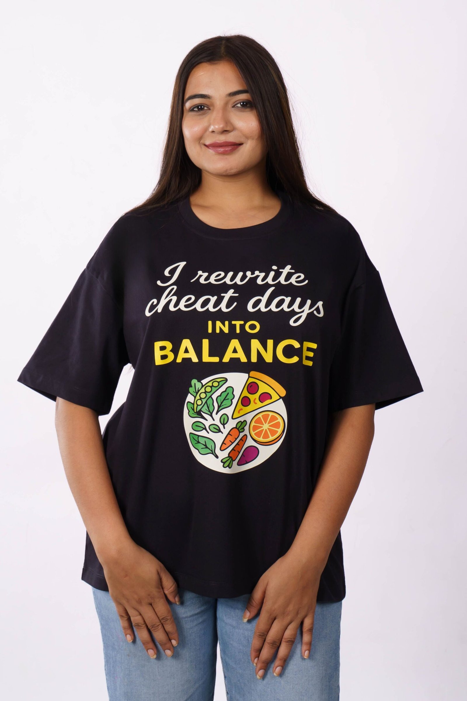 Smiling woman wearing oversized printed t-shirt promoting cheat day balance in Delhi studio.
